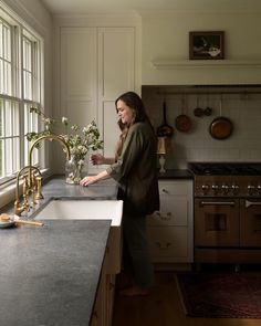 a woman standing in a kitchen next to a sink with a faucet on it