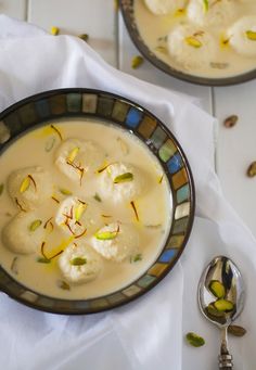 two bowls filled with food sitting on top of a white table next to spoons