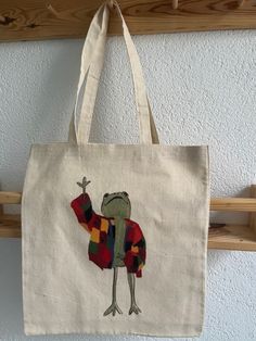 a tote bag with a frog on it hanging from a coat rack in a room