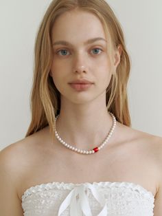 a woman wearing a white dress with a red beaded necklace