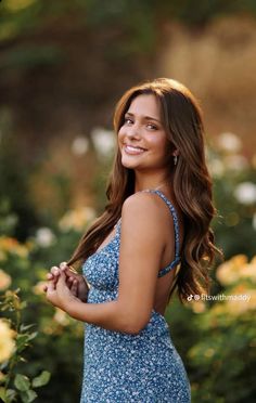 a beautiful young woman in a blue dress posing for the camera with flowers behind her