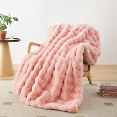 a pink blanket sitting on top of a wooden chair next to a potted plant