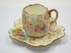 a cup and saucer sitting on top of a white tablecloth covered plate with floral designs