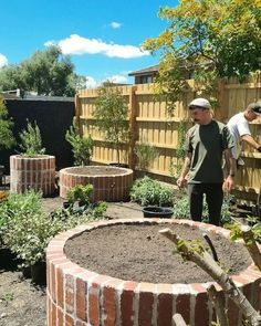 two men are standing in the middle of a garden with brick walls and raised planters