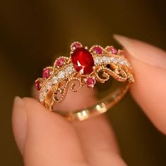 a woman's hand holding a ring with a red stone and white diamonds on it