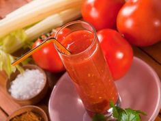 a glass filled with liquid sitting on top of a pink plate next to some vegetables