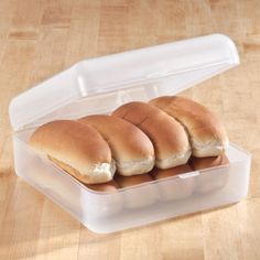 four hot dogs in a plastic container on a wooden table with one bun cut in half