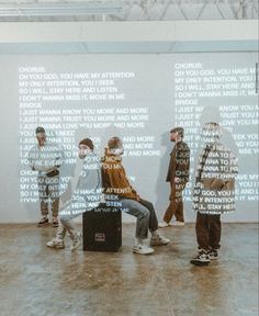 four people standing in front of a wall with words on it and one person sitting down