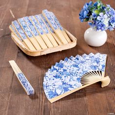 a blue and white fan next to a vase with flowers in it on a wooden table