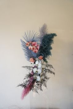 a vase filled with flowers and feathers sitting on top of a wooden table next to a wall