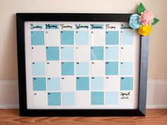 a blue and white framed calendar sitting on top of a wooden table next to a vase with flowers