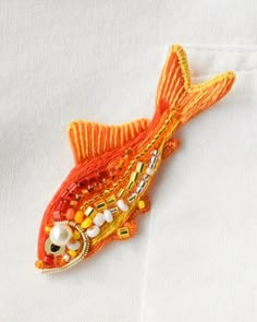 an orange fish brooch sitting on top of a white t - shirt with beads