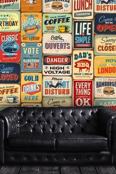 a black leather couch sitting in front of a wall covered with vintage metal tin signs