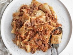 a white plate topped with pasta covered in meat and sauce next to a silver spoon