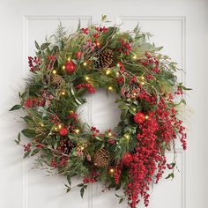 a christmas wreath with red berries, pine cones and greenery hangs on a white door