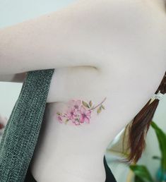 a woman's lower back tattoo with pink flowers on her left side ribcage