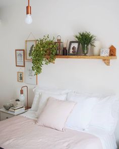 a bed with white sheets and pillows in a bedroom next to a plant on the wall