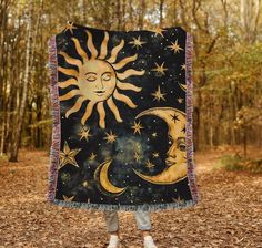 a woman standing in the woods holding up a blanket that has a sun and moon on it