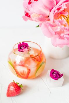 a vase filled with pink flowers and strawberries next to ice cubes on a white surface