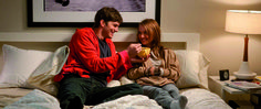 a man and woman sitting on top of a bed next to each other holding coffee cups