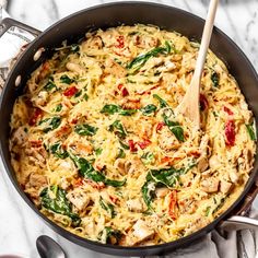 a skillet filled with pasta and spinach on top of a marble countertop