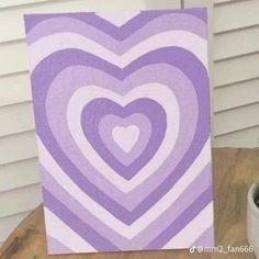 a purple and white heart painting sitting on top of a table next to a potted plant