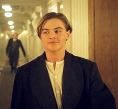 a young man in a suit and tie walking down a hallway next to another person