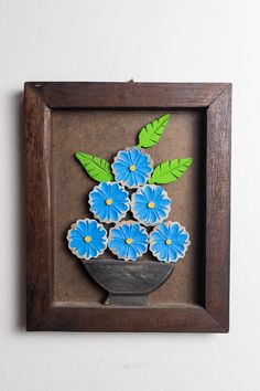 a wooden frame with blue flowers and green leaves on the inside, hanging on a wall