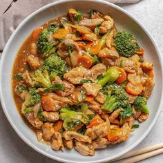 a white bowl filled with chicken and broccoli stir fry next to chopsticks