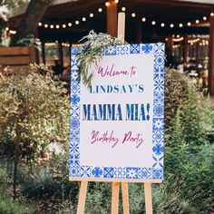 a welcome sign for a birthday party in front of a building with lights and greenery