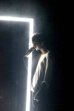 a man standing in front of a microphone on top of a stage with lights behind him