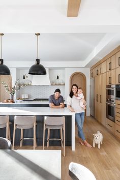 a man and woman standing in a kitchen next to a dog