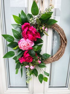 a wreath with pink flowers and greenery hangs on the front door