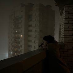 a woman leaning on a ledge looking out at the city in the foggy night