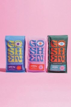 three bags of coffee sitting next to each other on a pink background