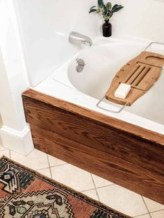 a bath tub with a wooden seat on top of it next to a rug and potted plant