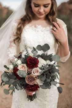 a woman in a wedding dress holding a bridal bouquet with red and white flowers