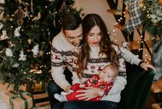 a man and woman holding a baby in front of a christmas tree