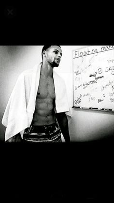 a shirtless man standing in front of a whiteboard with writing on it and looking at the camera