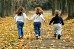 two young children walking down a leaf covered path