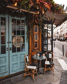 two chairs sitting at a table in front of a building with blue doors and windows