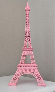 a pink model of the eiffel tower on a white shelf in front of a gray wall