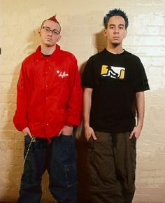 two men standing next to each other in front of a brick wall with chains on it