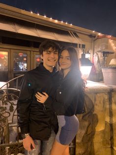 a man and woman standing next to each other in front of a building at night