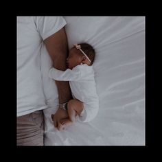 a man holding a sleeping baby on top of a white bed next to his arm