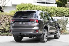 the rear end of a gray ford explorer parked in front of a building with bushes