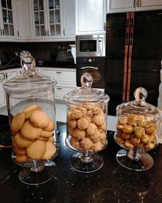 three glass jars filled with cookies sitting on top of a counter next to an oven