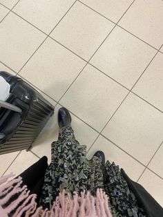 a person standing next to a piece of luggage on top of a tiled floor in front of a mirror