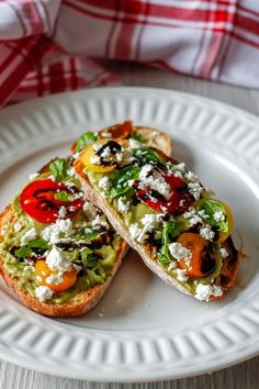 two pieces of bread with vegetables and cheese on them sitting on a white plate next to a red checkered napkin