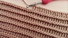 the crochet stitch is being worked on by a pink handled knitting needle, along with a pair of scissors